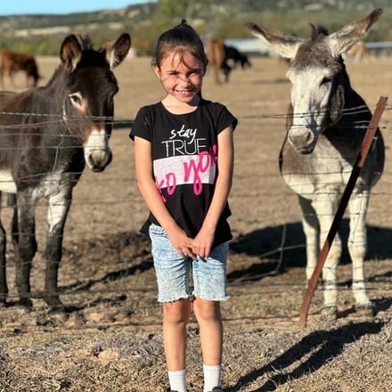 Girl smiling between two miniature donkeys at the fence