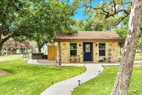 Stone cottage with dark blue door surrounded by mature oak trees and manicured lawn